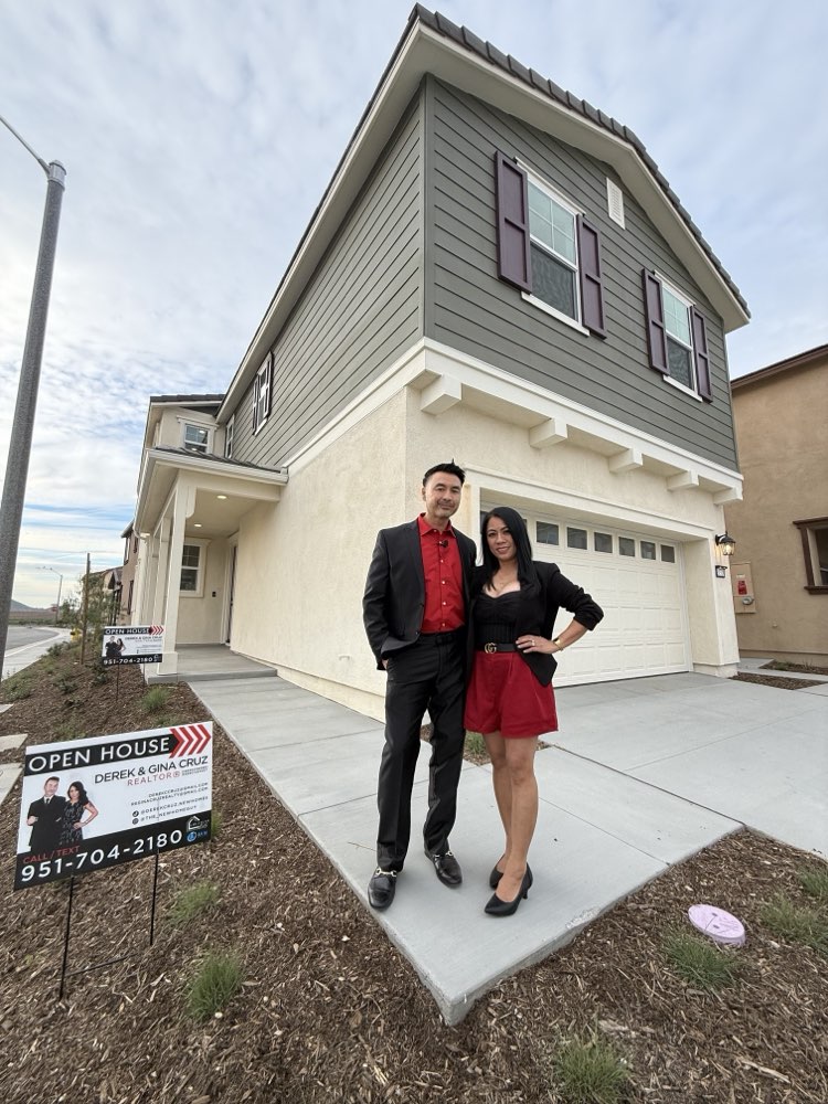 Derek and Gina Cruz in front of a new-construction open house with their Cruz Team Realty sign